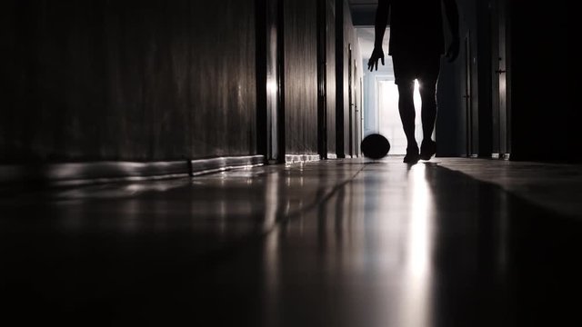 Rear view of silhouette of sportsman walking along hallway and dribbling basketball 