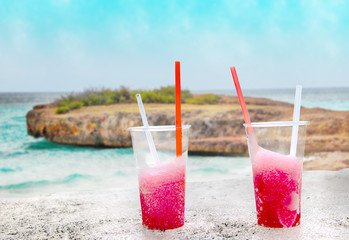 Two strawberry red drift-ice with straw on the beach. In the background is blue sky, sea nd sandy beach. This is situated in tropical resort in Caribbean. © Jana