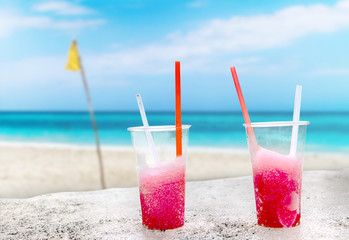 Two strawberry red drift-ice with straw on the beach. In the background is blue sky, palms, sea nd sandy beach. This is situated in tropical resort in Caribbean. © Jana