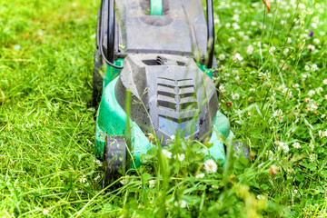 Man cutting green grass with lawn mower in backyard. Gardening country lifestyle background. Beautiful view on fresh green grass lawn in sunlight, garden landscape in spring or summer season