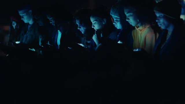 group of friends using smartphone mobile technology hanging out on rooftop at night enjoying weekend sharing social media messages addiction concept