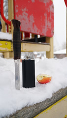 Winter still life with the knife, the black flask and apple in the snow