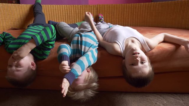 Three happy blond boys ate lots of candy. Children's tongue turned blue from marmalade. Striped home pajamas, proton purple background, sofa. Children have good time together.