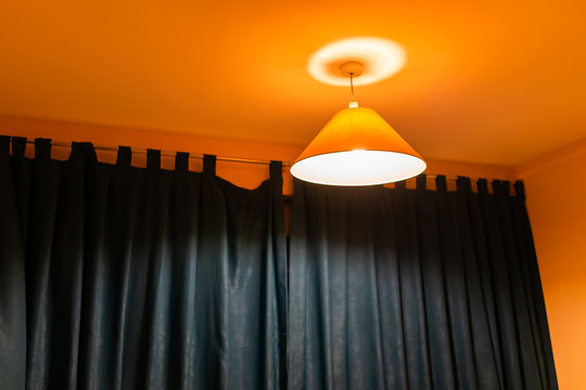 Decorative Yellow Orange Lamp Hanging On Ceiling Illuminated During Evening Night, Colorful Light, In Bedroom Home, House Apartment With Dark Window Blinds Curtains