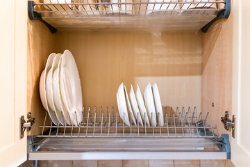 Open light yellow wooden kitchen cabinet door cupboard with many white and clean dishes, plates and cups on shelves closeup