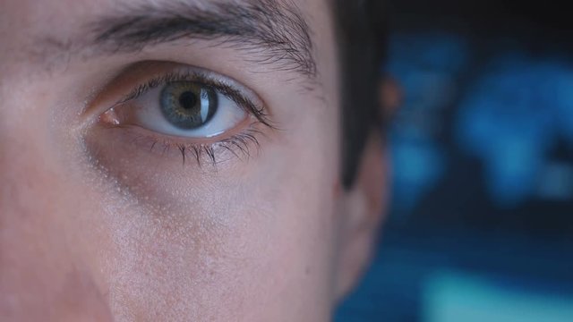 Close-up Eye in macro of a Male Programmer Geek in a data center filled with monitor screens