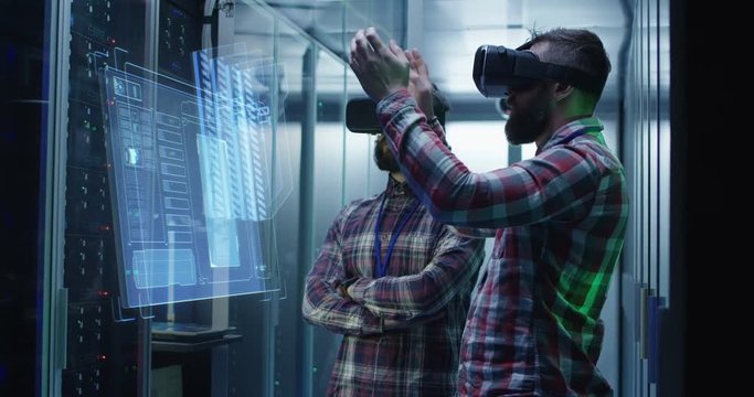 Medium shot of two male technician in VR glasses using a virtual interface while working in a data center