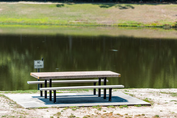 Obraz premium Rest area stop with lake pond by highway road in North Carolina with empty picnic table in park and no fishing sign during day