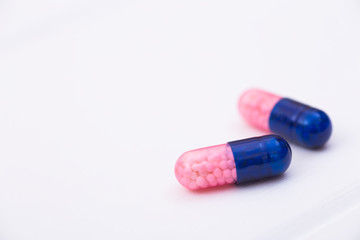 Closeup two dark blue and pink transparent capsules with micro-granules inside on white background