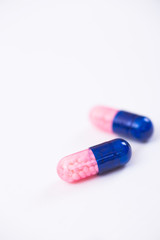 Closeup two dark blue and pink transparent capsules with micro-granules inside on white background