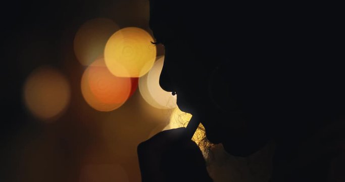  silhouette of woman applying lipstick makeup in city at night preparing for evening party with bokeh lights in background