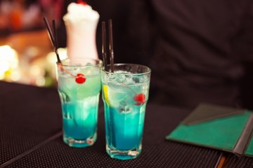 Blue lagoon cocktail classic cocktails on bar. Close-up cold cocktail with crushed ice and slice of lemon on glass. Guest check presenter book at background