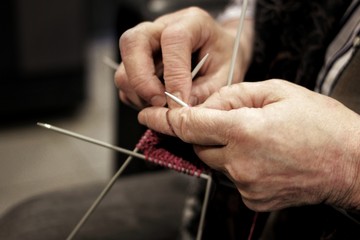 The hands of an elderly woman knit clothes out of wool yarn with knitting needles