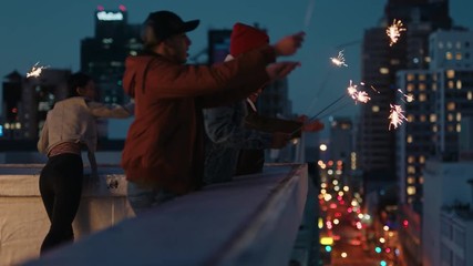 happy friends holding sparklers celebrating new years eve on rooftop at sunset having fun enjoying holiday party celebration