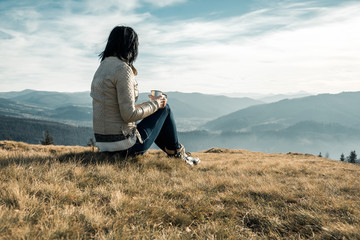 girl with a metal cup sits on a background of mountains
