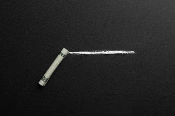 Line of cocaine and rolled money bill on dark background, top view