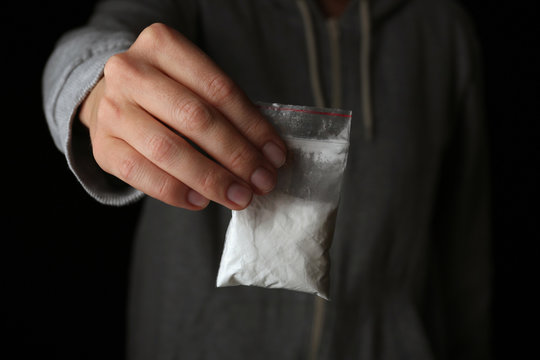 Drug dealer holding bag with cocaine on black background, closeup