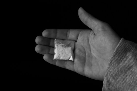 Drug dealer holding bag with cocaine on black background, closeup