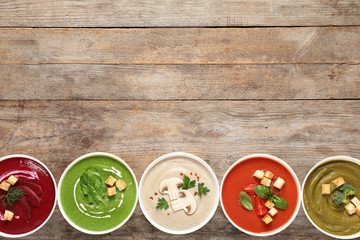 Various cream soups in bowls and space for text on wooden background, top view