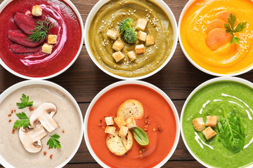 Various cream soups in bowls on wooden background, top view