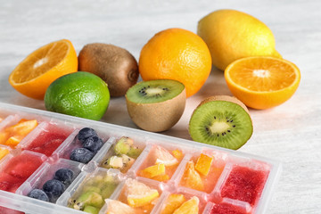 Ice cubes with fruits and berries in tray near ingredients on light table