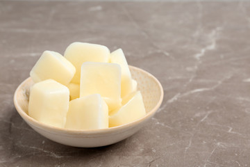 Bowl with milk ice cubes on grey table. Space for text
