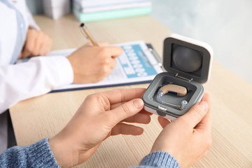 Patient with hearing aid in box and blurred doctor on background, closeup