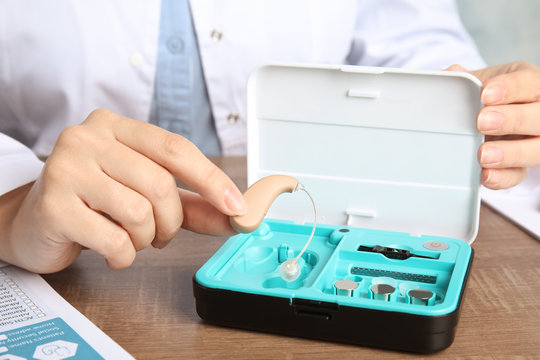 Doctor putting hearing aid into box at table, closeup. Medical device