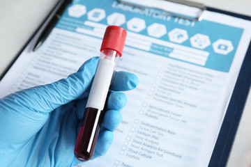 Laboratory worker holding test tube with blood sample for analysis beside medical form, closeup