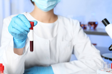 Laboratory worker holding test tube with blood sample for analysis, closeup