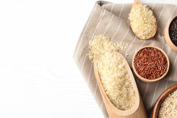 Flat lay composition with brown and other types of rice on white wooden background. Space for text