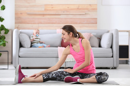 Young sportive woman doing exercise while her son sitting on sofa at home. Fitness training