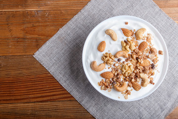 White plate with greek yogurt, granola, almond, cashew, walnuts  on brown wooden background.