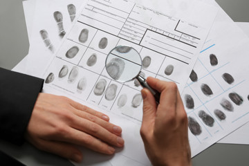 Female criminalist exploring fingerprints with magnifier at table, closeup