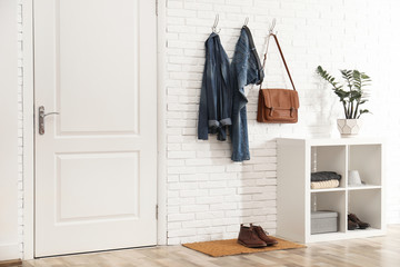 Obraz na płótnie Canvas Stylish hallway interior with door, comfortable furniture and clothes on brick wall