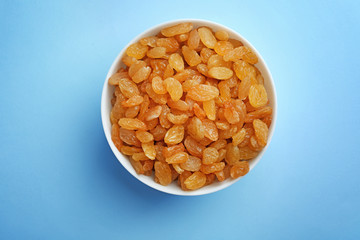 Bowl with raisins on color background, top view. Dried fruit as healthy snack