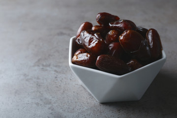 Bowl with sweet dates on grey background, space for text. Dried fruit as healthy snack