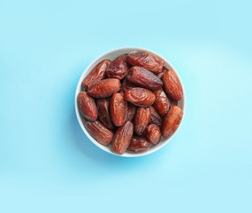 Bowl with sweet dried date fruits on color background, top view