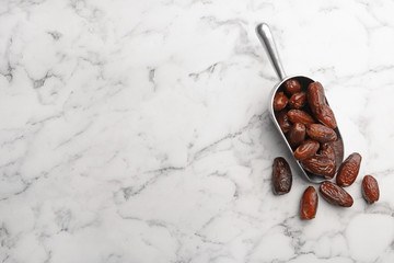 Scoop with sweet dried date fruits on marble background, top view. Space for text