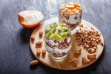 dessert with greek yogurt, granola, almond, cashew, kiwi and persimmon on wooden background.