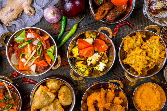 Assorted indian food set on wooden background. Dishes and appetisers of indeed cuisine, rice, lentils, paneer, samosa, spices, masala. Bowls and plates with indian food