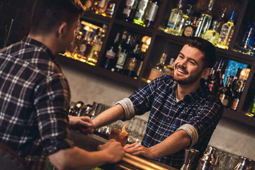 Young bartender standing at bar counter with customer talking happy