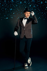 Professional Occupation. Showman in suit gloves and hat standing isolated on wall with cane posing...