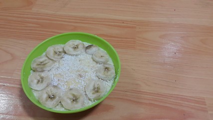 Creamy tasty sweet custard with banana pieces on surface inbowl on wooden floor