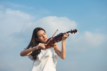 Beautiful asia girl with black hair and white dress playing on a violin © sutlafk