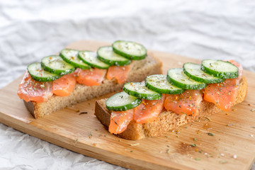 sandwiches with bread, fresh fish and sliced cucumbers with spices on wooden tray