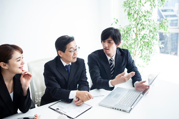 三人の会社員がパソコンを見ながら意見を交わしている