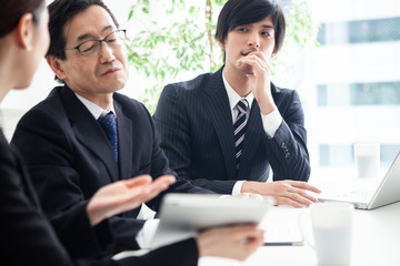 男性会社員がタブレットを見ながら説明を受けているシーン