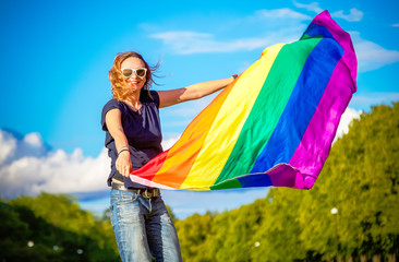Young happy woman in a summer park with a rainbow flag in her hands, the symbol of LGBT, equal...