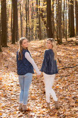 Naklejka na ściany i meble Two stunning young women friends walk through autumn woods holding hands
